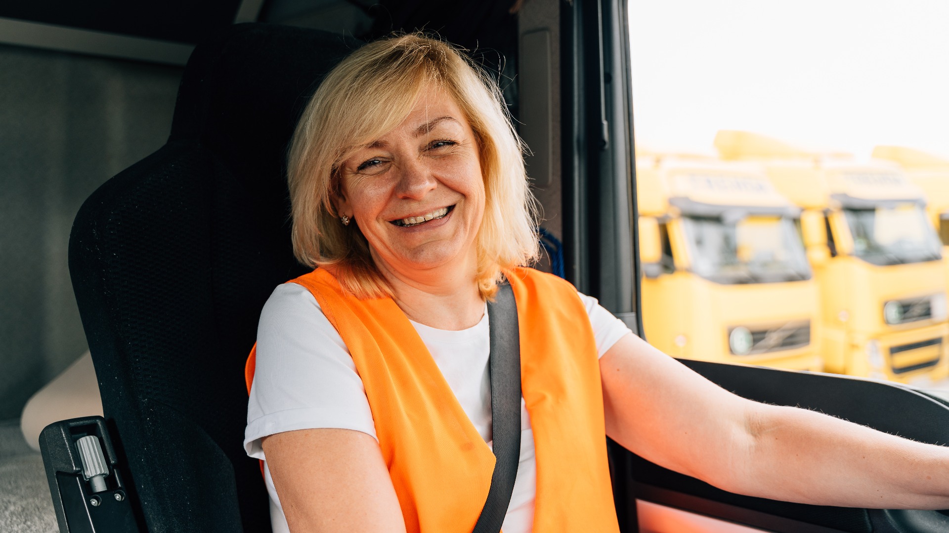 Eine LKW-Fahrerin am Lenkrad in LKW-Kabine.